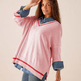 Pink and red V-neck knit sweater featuring oversized sleeves and a relaxed fit over a denim shirt.