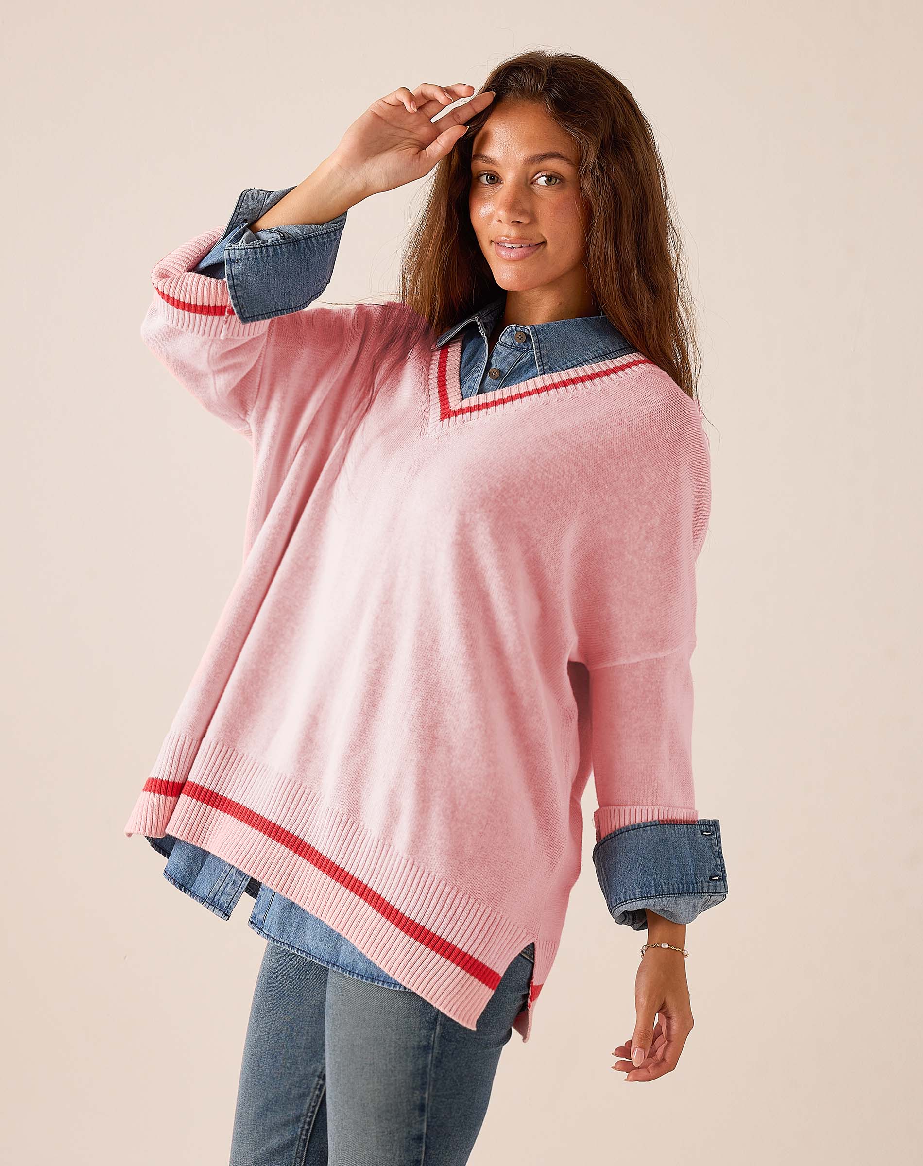 Pink and red V-neck knit sweater featuring oversized sleeves and a relaxed fit over a denim shirt.