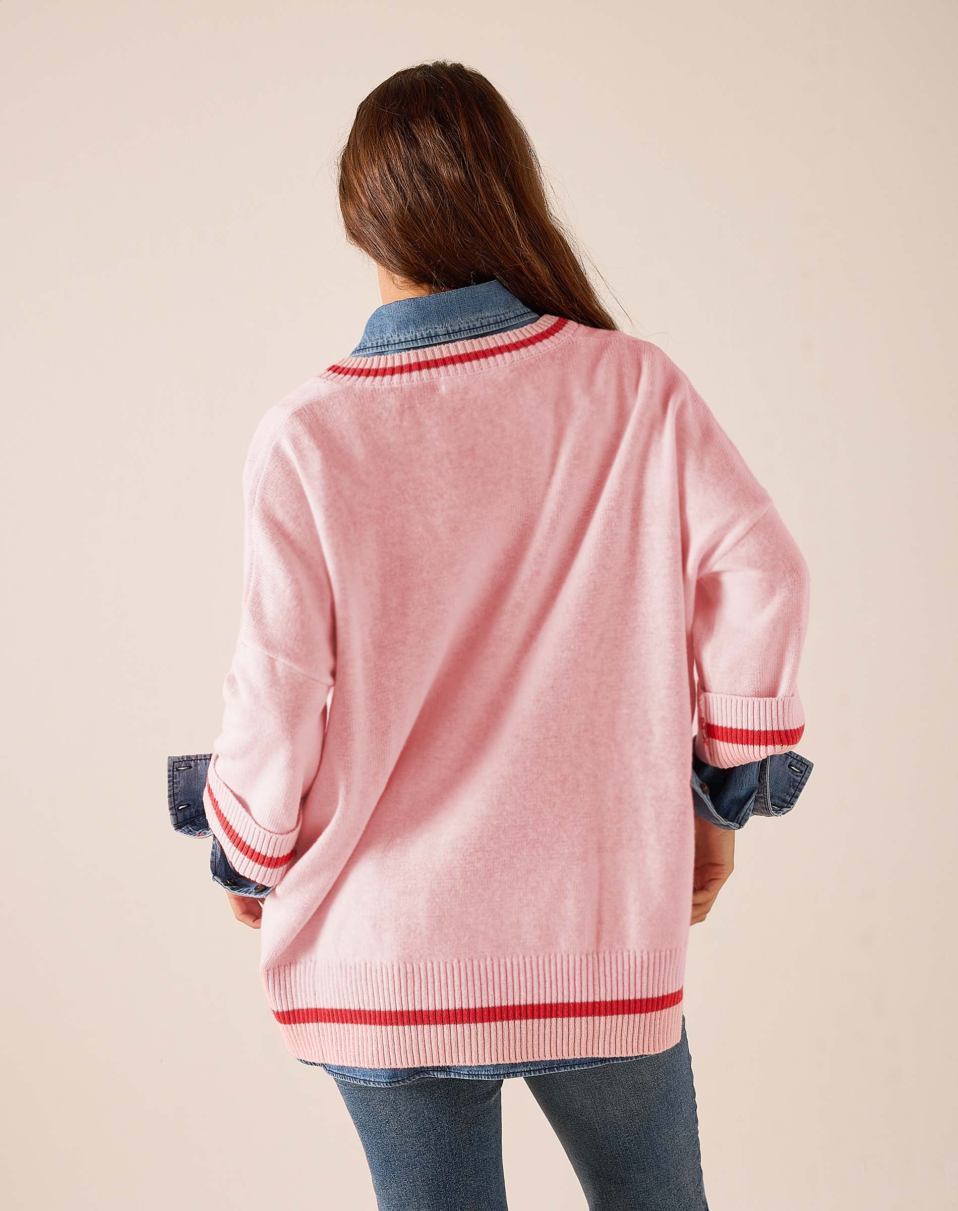 Back view of women's travel-friendly pink and red knit v-neck pullover with a striped hem and contrasting blue denim-style collar detail.