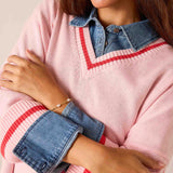 Pink knit V-neck sweater with red stripe detail and a layered denim shirt.