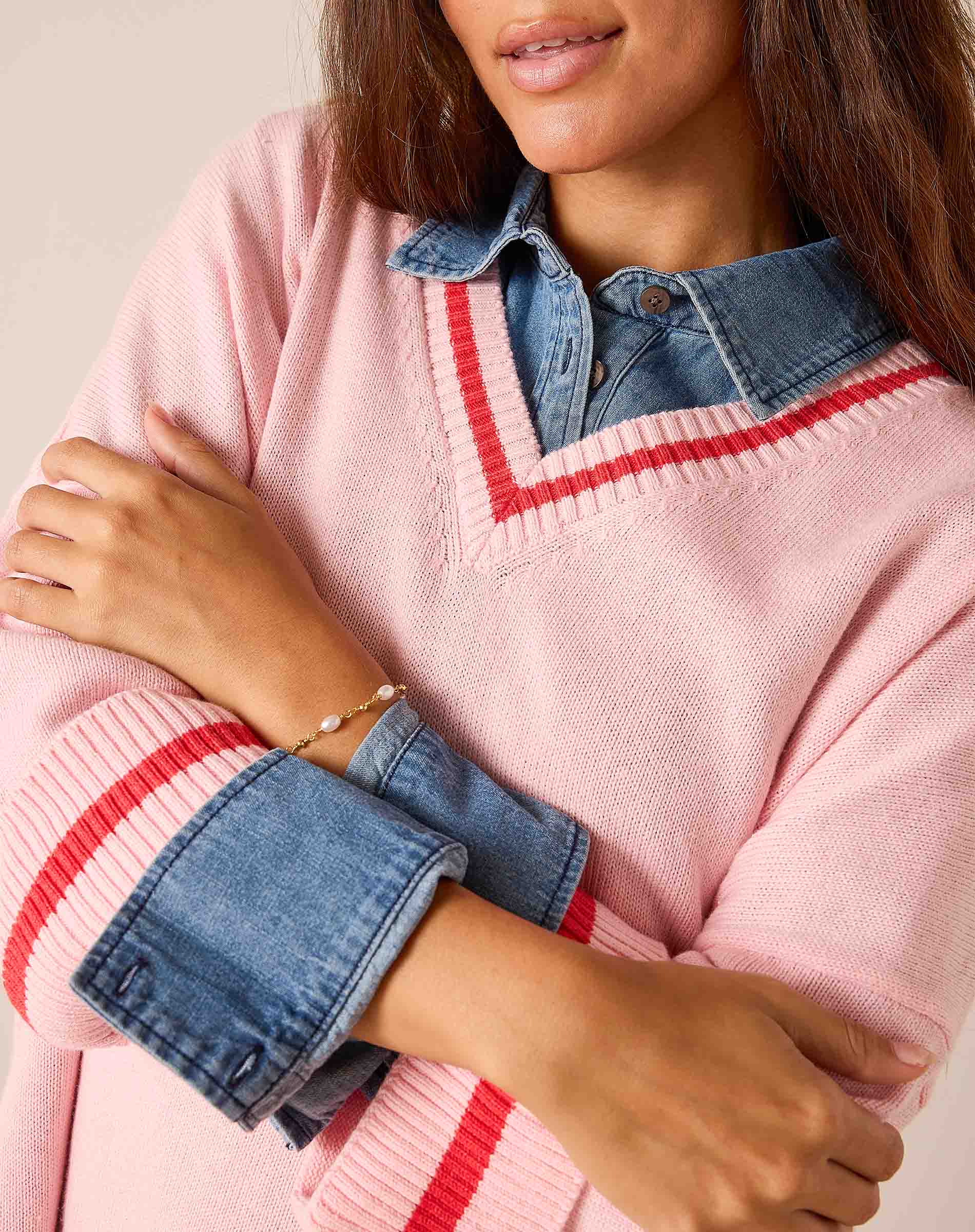 Pink knit V-neck sweater with red stripe detail and a layered denim shirt.