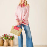 Woman in pink sweater and blue jeans holding a straw bag with red handle.