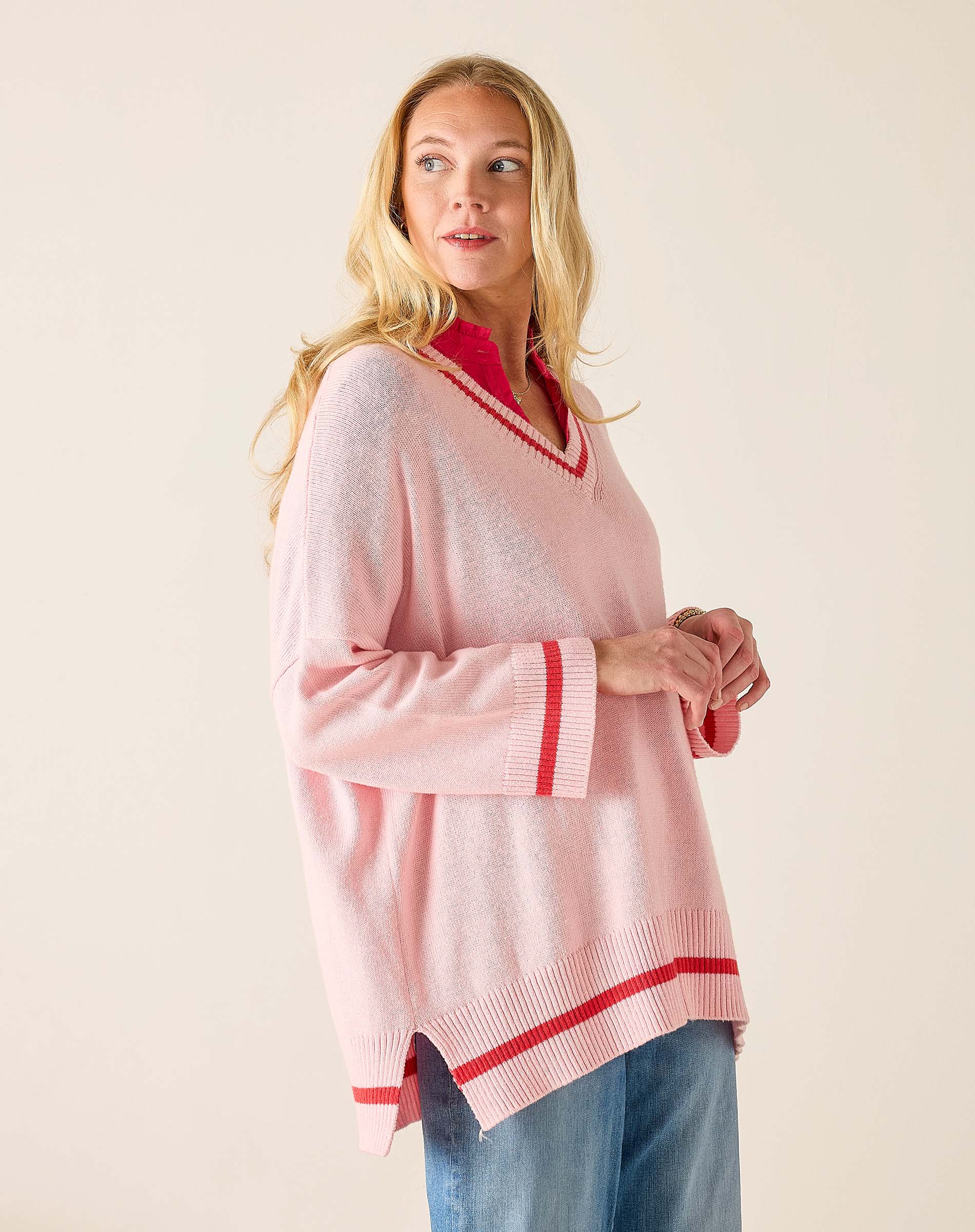 Woman wearing a pink sweater with red trim on a plain background
