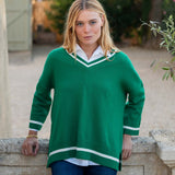 Woman wearing a green sweater with white trim standing outdoors.