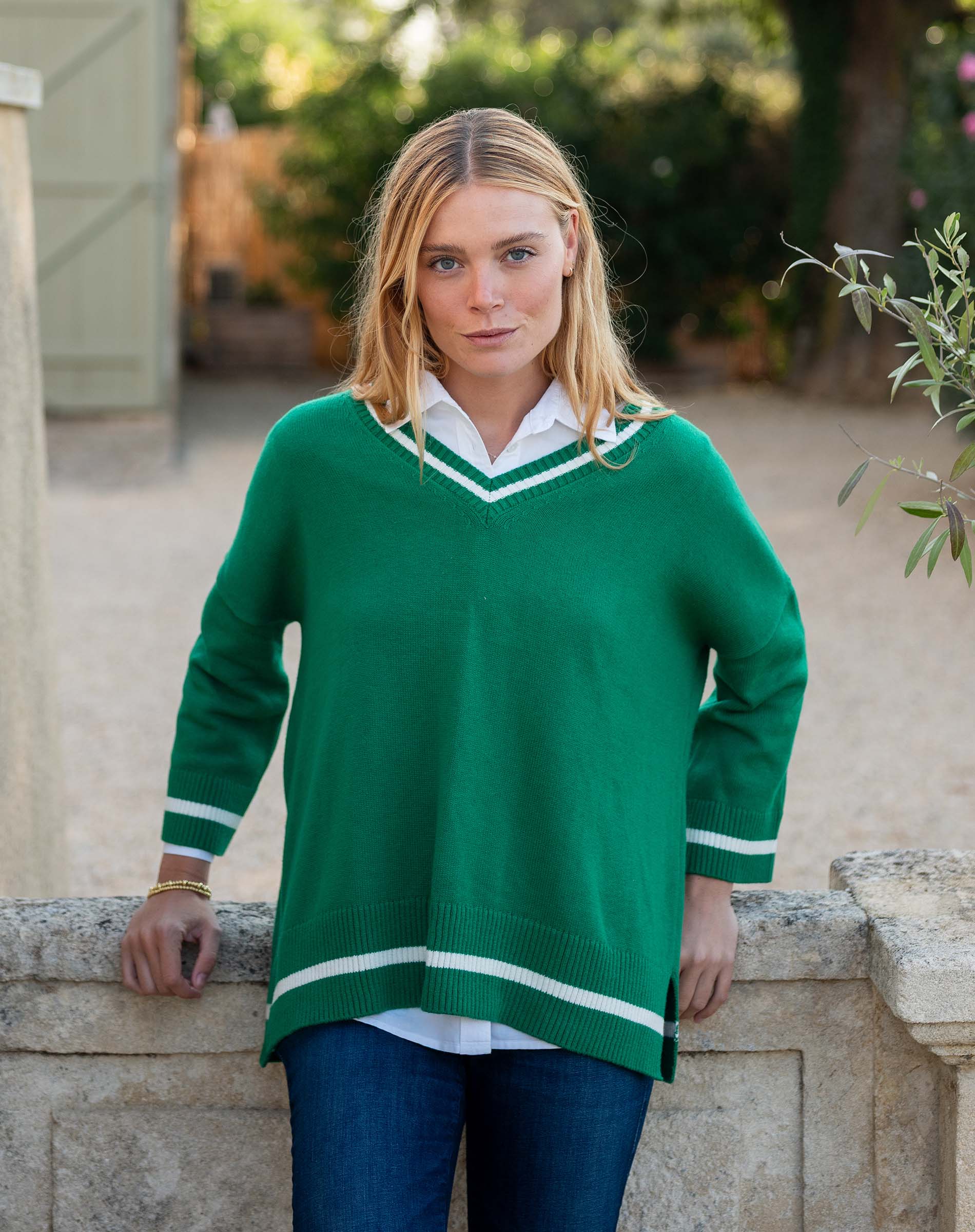 Woman wearing a green sweater with white trim standing outdoors.
