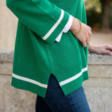 Green sweater with white stripes worn by a person, blurred background