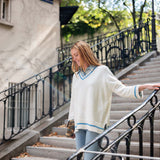 Woman in a white sweater with blue trim standing on outdoor steps.