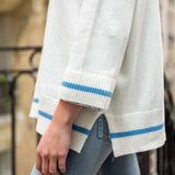 Light gray sweater with blue stripes on cuffs and hem worn by a person outdoors.