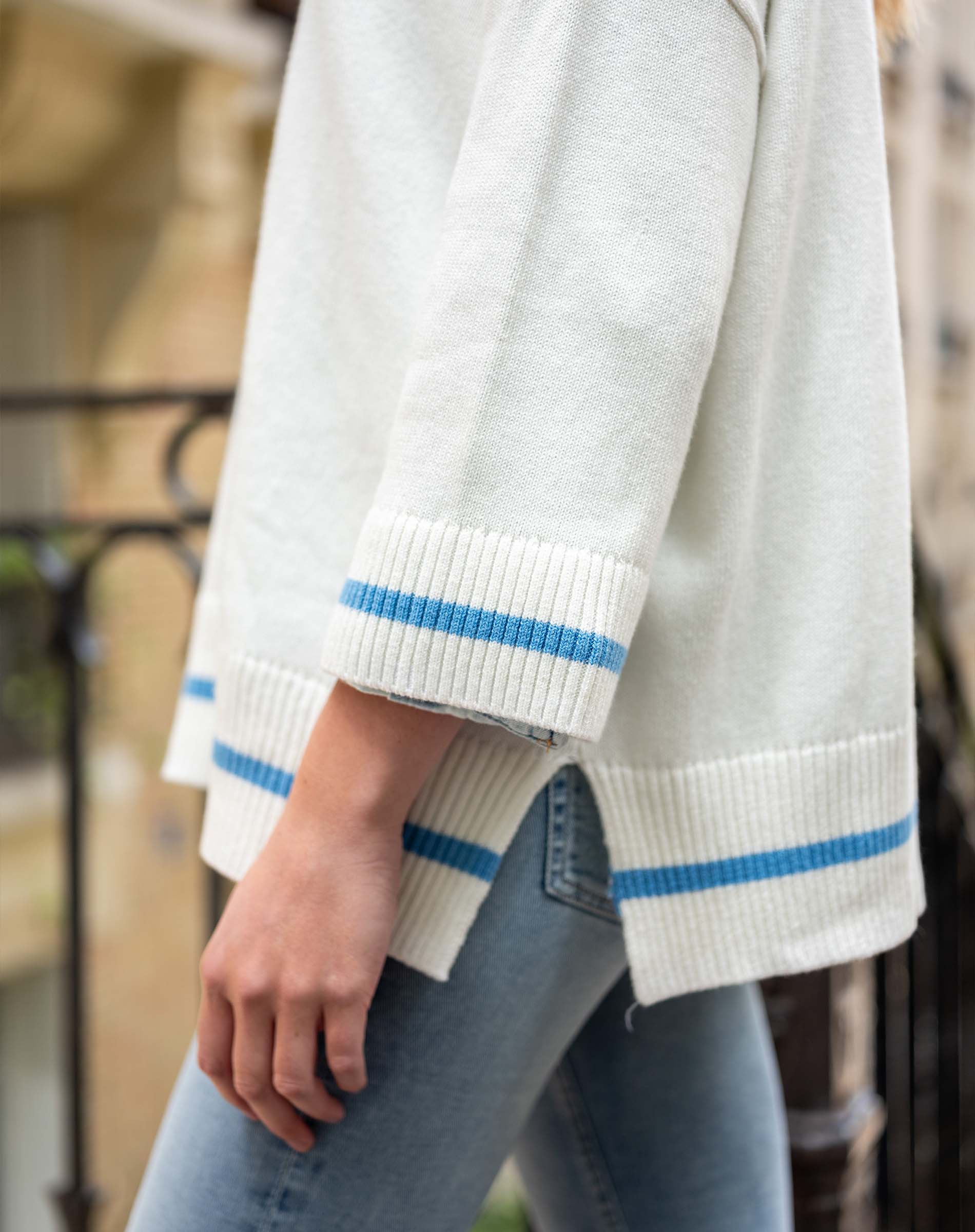 Light gray sweater with blue stripes on cuffs and hem worn by a person outdoors.