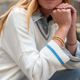 Person wearing a white sweater with blue accents and gold bracelets.