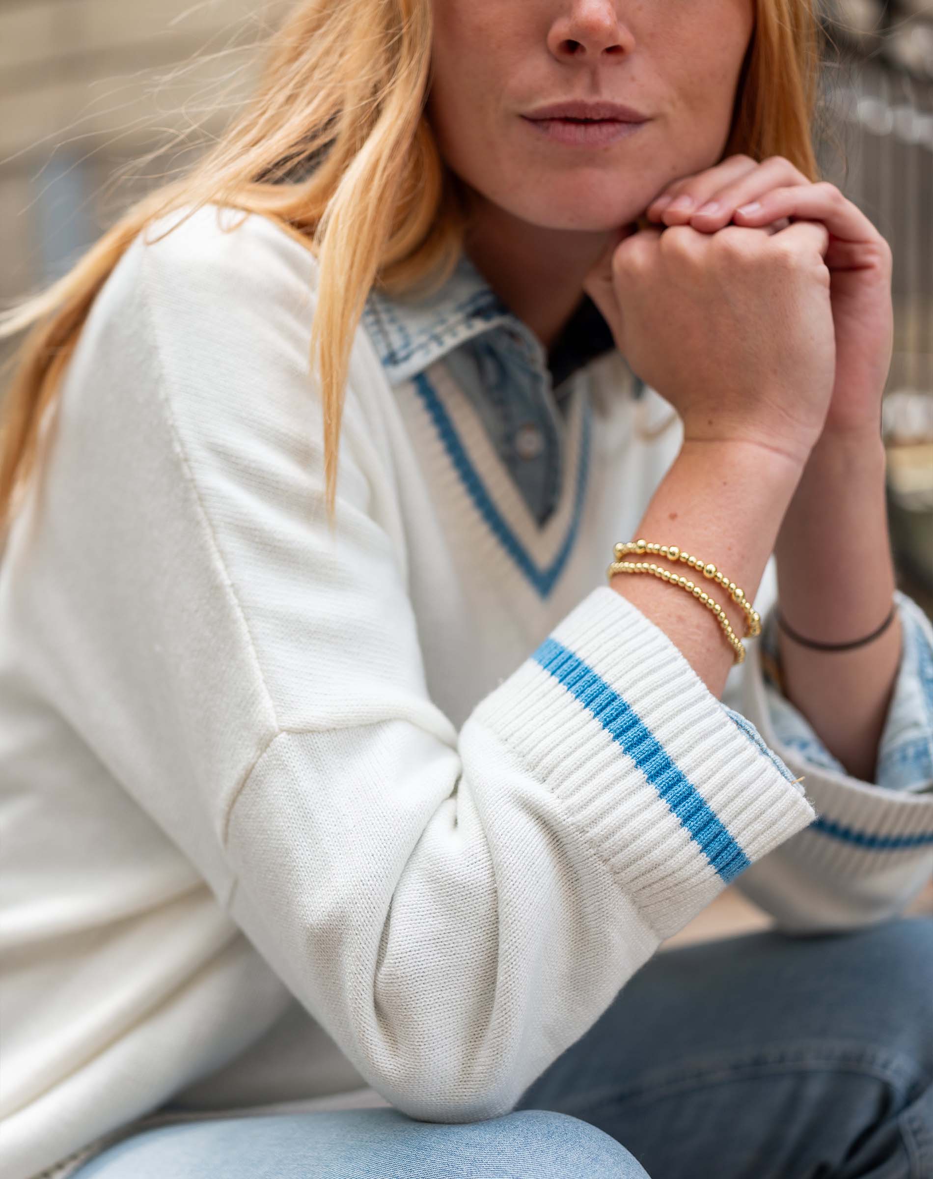 Person wearing a white sweater with blue accents and gold bracelets.