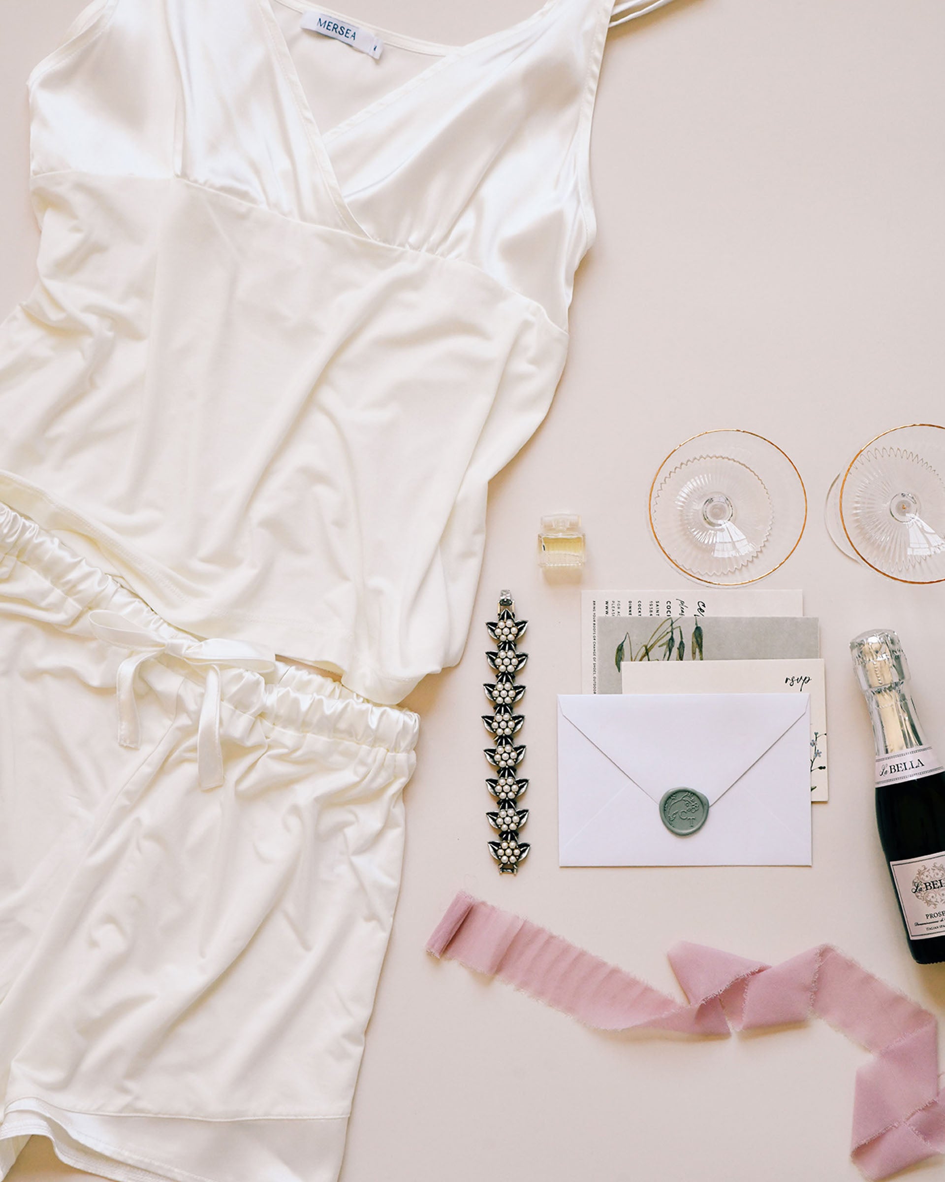 flat lay of white pajama silk tank and matching shorts next to champagne, save the date, & glasses