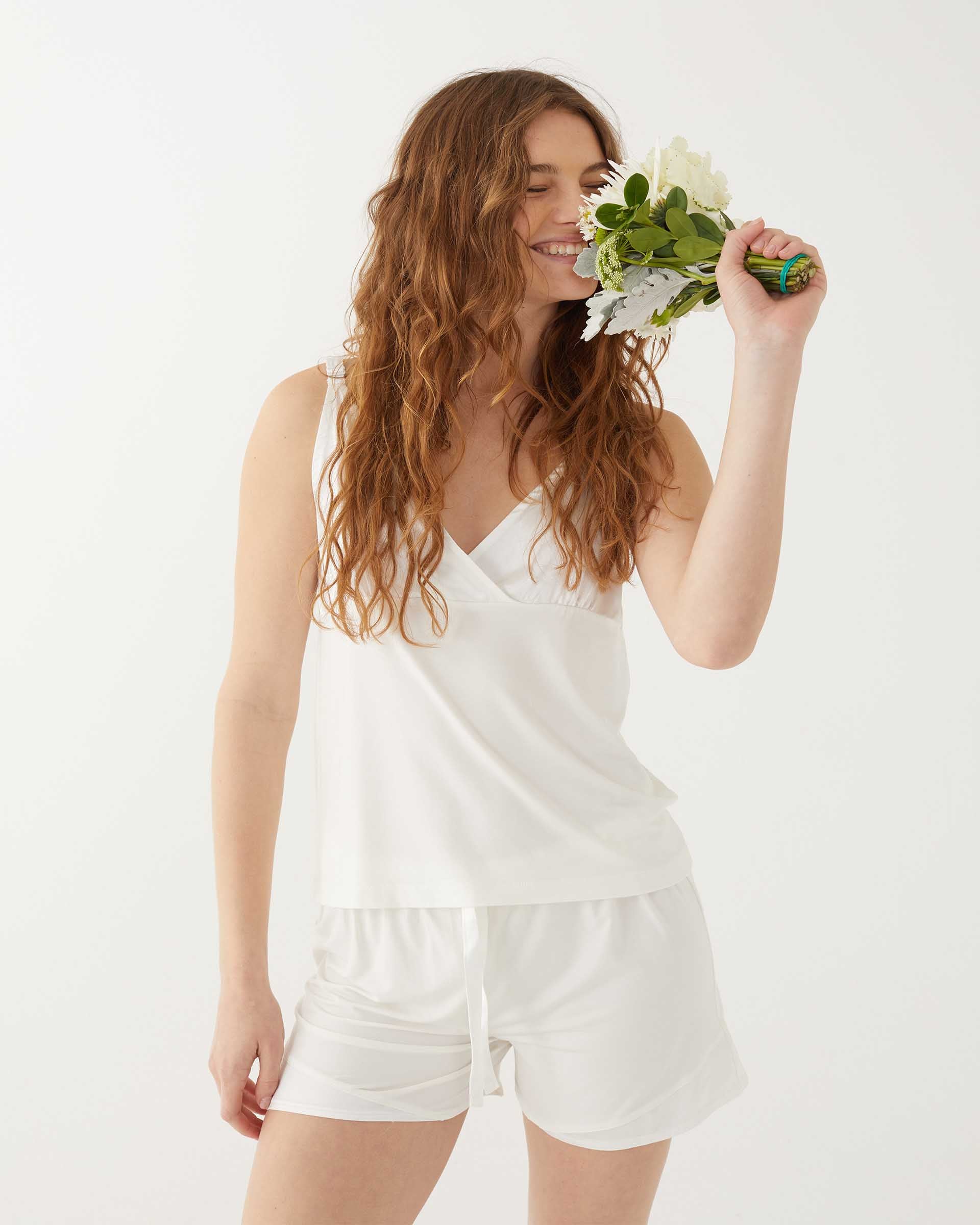 female wearing white pajama silk tank and matching shorts holding flowers on a white background