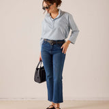 MERSEA ladies' travel-ready light blue button-down linen shirt with a relaxed fit and collar, paired with blue denim jeans and a black leather belt.