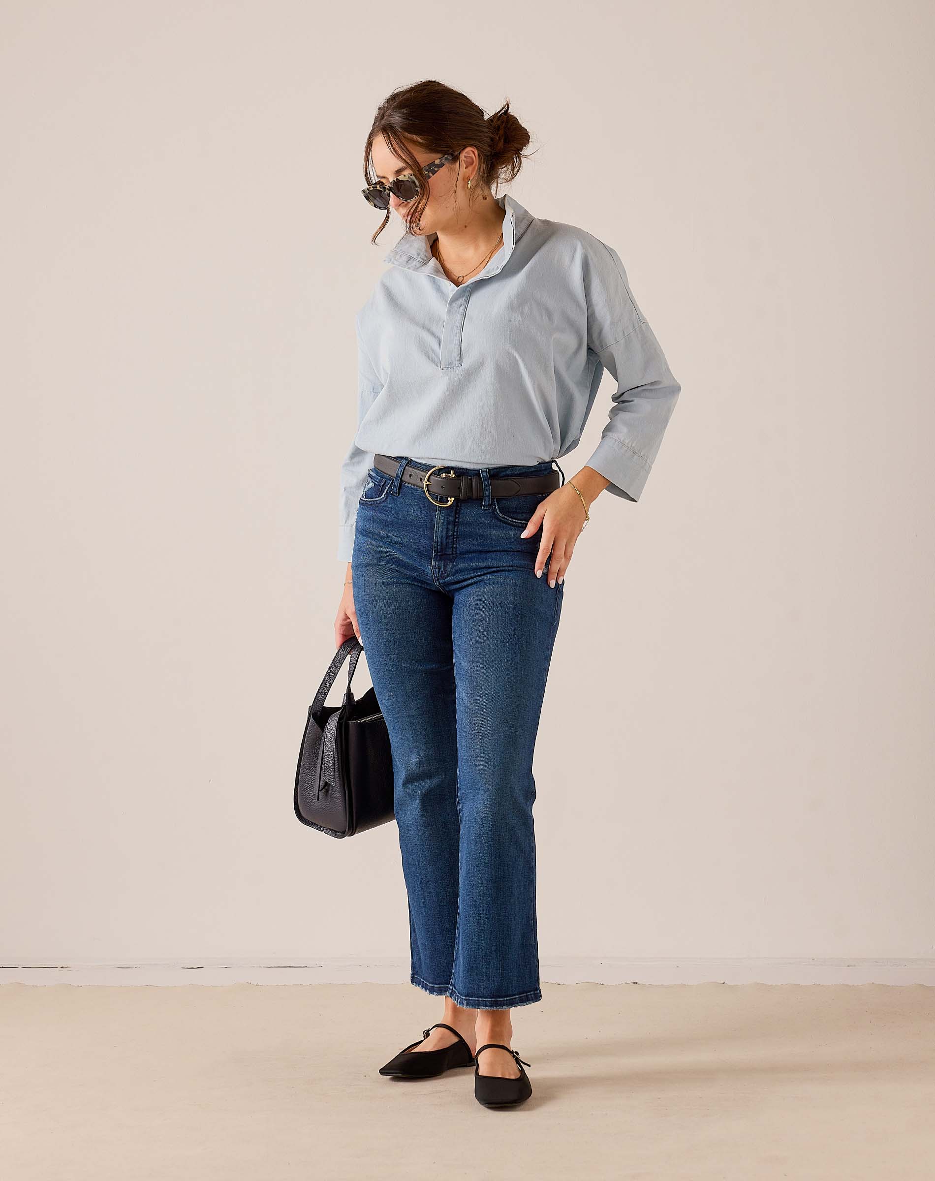 MERSEA ladies' travel-ready light blue button-down linen shirt with a relaxed fit and collar, paired with blue denim jeans and a black leather belt.