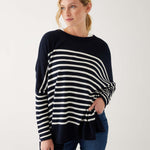 female wearing navy and white striped sweater with blue jeans on a white background