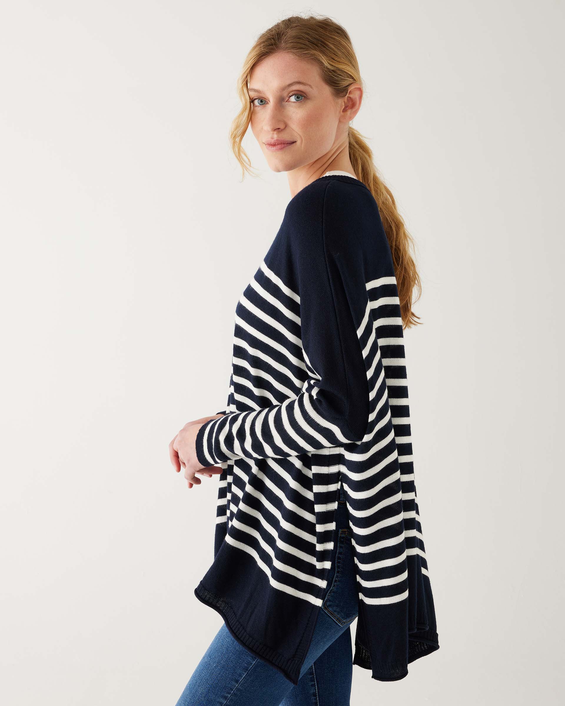 female wearing navy and white striped sweater with blue jeans sideways on a white background