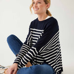 female wearing navy and white striped sweater with blue jeans sitting on a white background