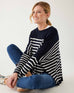 female wearing navy and white striped sweater with blue jeans sitting on a white background
