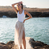 woman wearing lightweight mersea nellie wrap in neutral moonstone color wrapped around waist standing in front of body of water