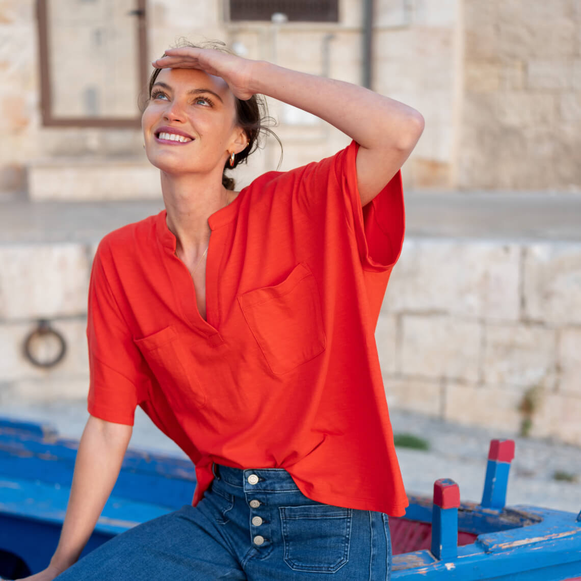 woman in orange top and jeans sitting on wooden boat out of water