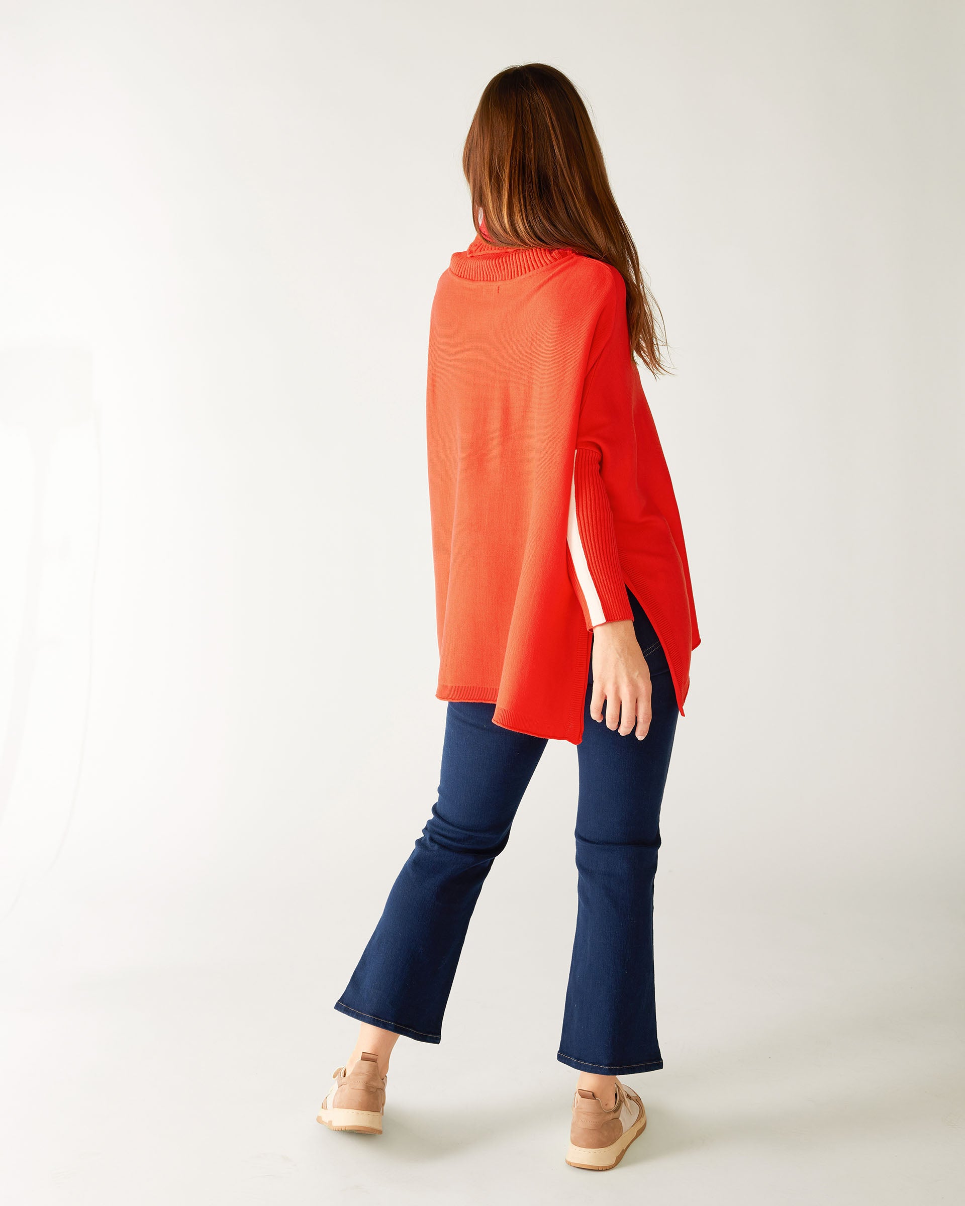 rearview of woman wearing mersea newport sweater in chili red with white accent stripe on lower sleeve , a split front turtleneck and ribbed sleeves.