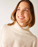 closeup of collar on woman wearing mersea newport sweater in salt storm white with grey accent stripe down lower sleeve with a split front turtleneck and ribbed sleeves
