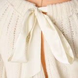 White chunky knit ribbed sweater with large decorative bow detail.