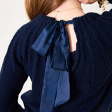Navy blue ribbed knit sweater with a large decorative satin ribbon tie at the back.