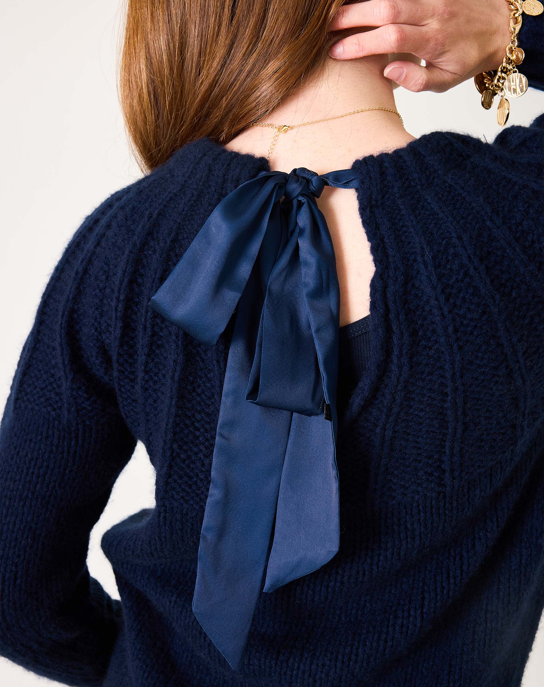Navy blue ribbed knit sweater with a large decorative satin ribbon tie at the back.