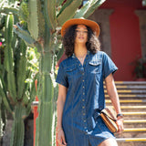 Woman in a blue dress and orange hat standing next to a cactus plant.