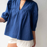 Person wearing a blue blouse and white shorts against a plain background