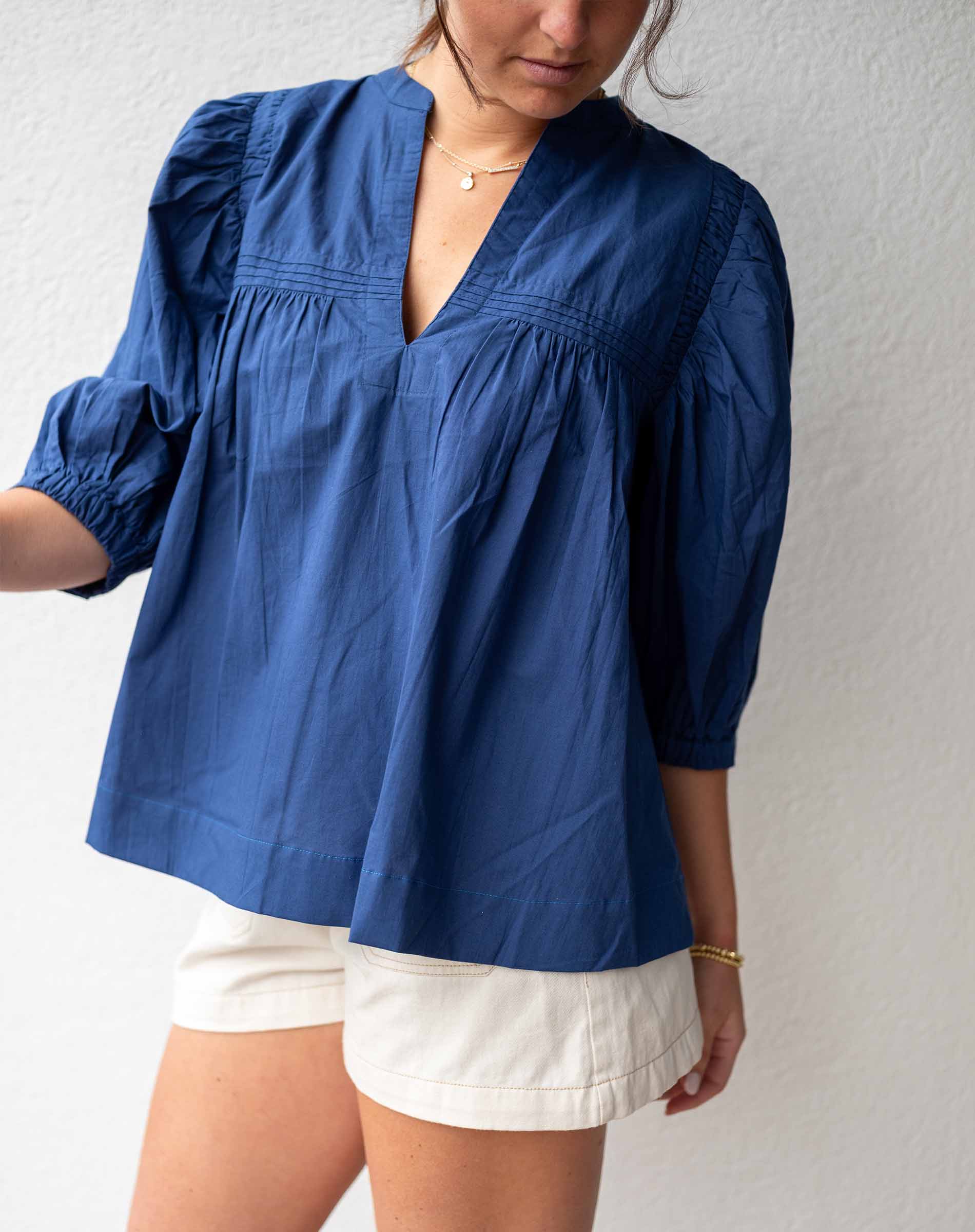 Person wearing a blue blouse and white shorts against a plain background