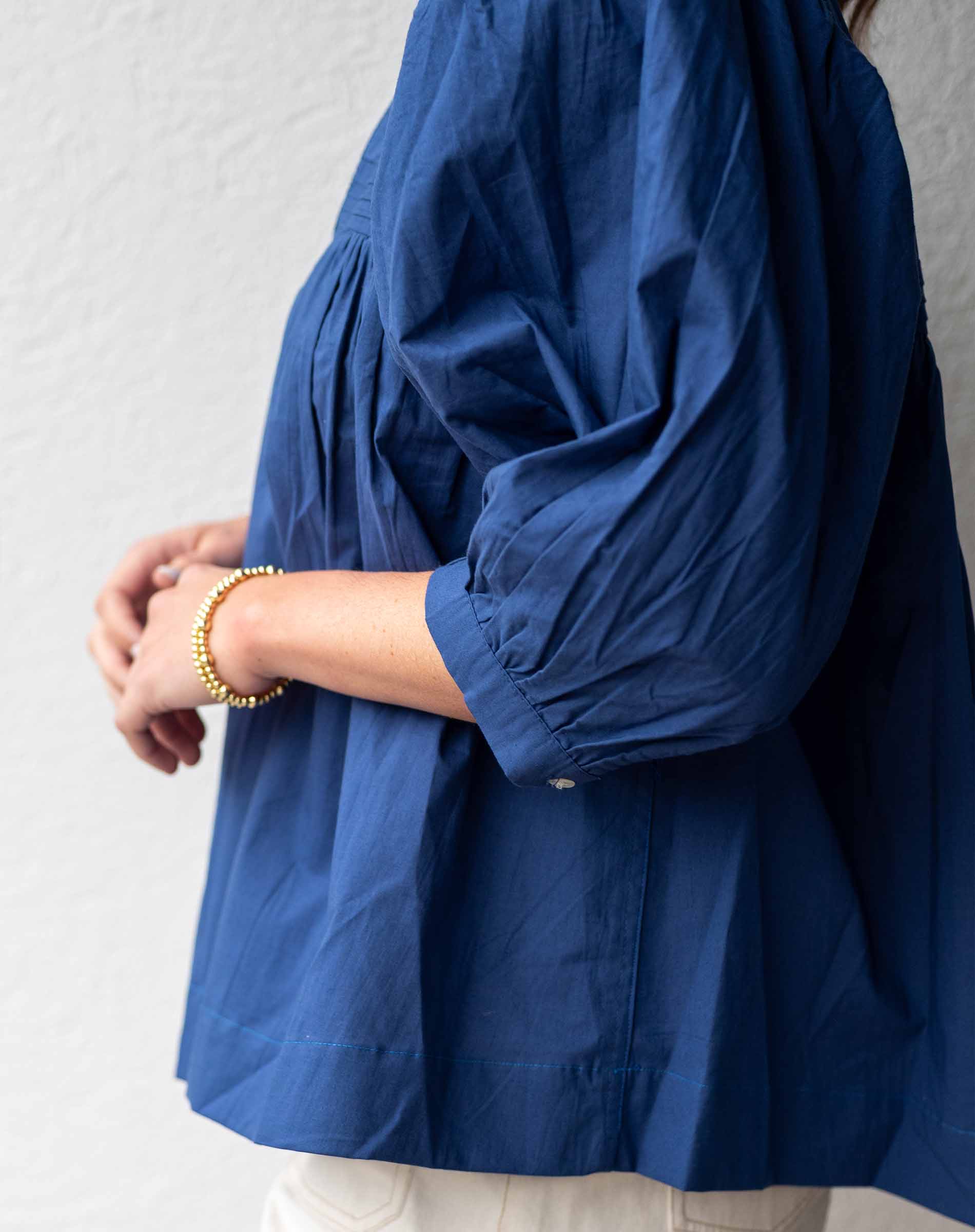 Person wearing a blue blouse with long sleeves against a plain background