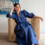Woman in a blue dress sitting on a wicker chair indoors.