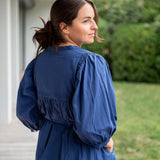 Woman wearing a blue dress standing outdoors with greenery in the background