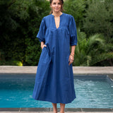 Woman in a blue dress standing by a pool with greenery in the background