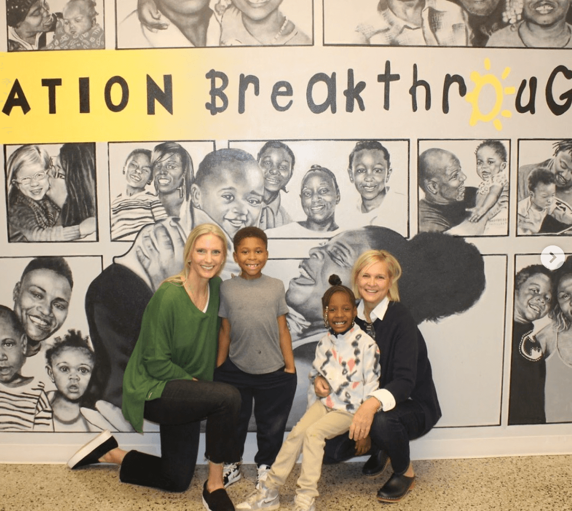 Two women and two children posing in front of a wall mural with children's faces.