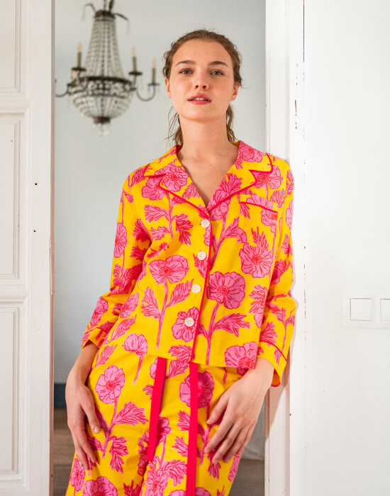 female wearing matching pajama set with yellow and pink floral print leaning against a doorway