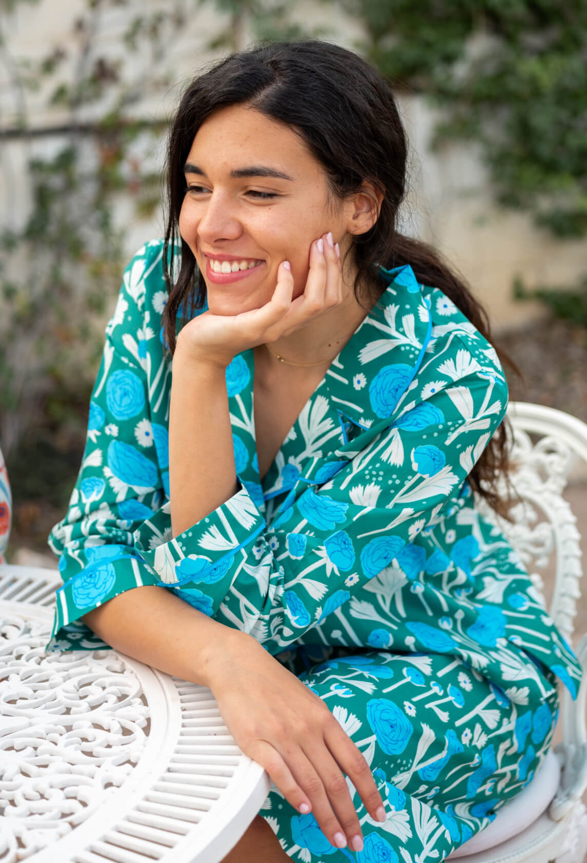 female wearing matching pajama set with green and blue floral print sitting by a white table