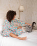 woman sitting on a bed petting a cat in over the cotton moon pjs in block print poppy pattern