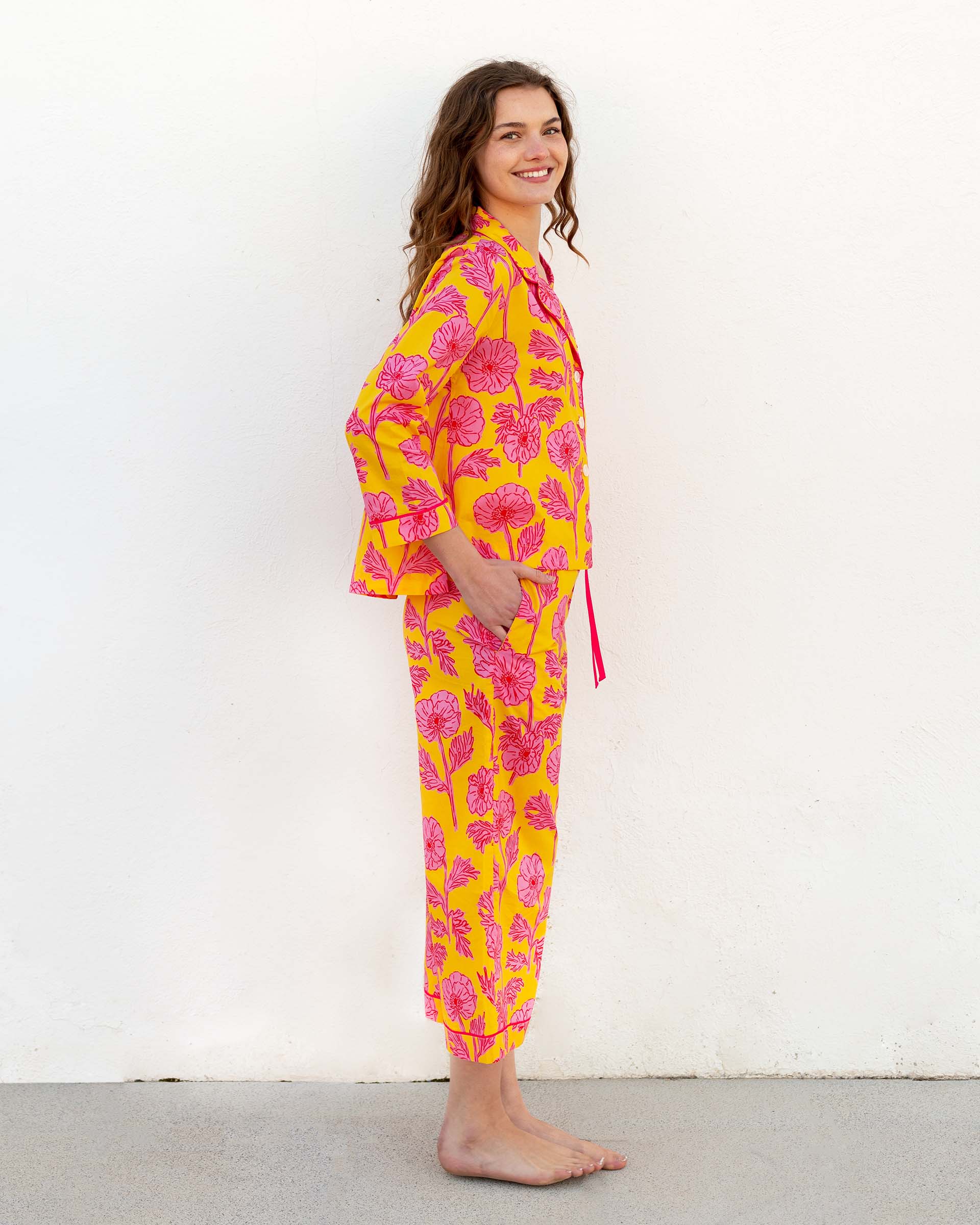 female wearing matching pajama set with pink poppy flower print sideways in front of white wall
