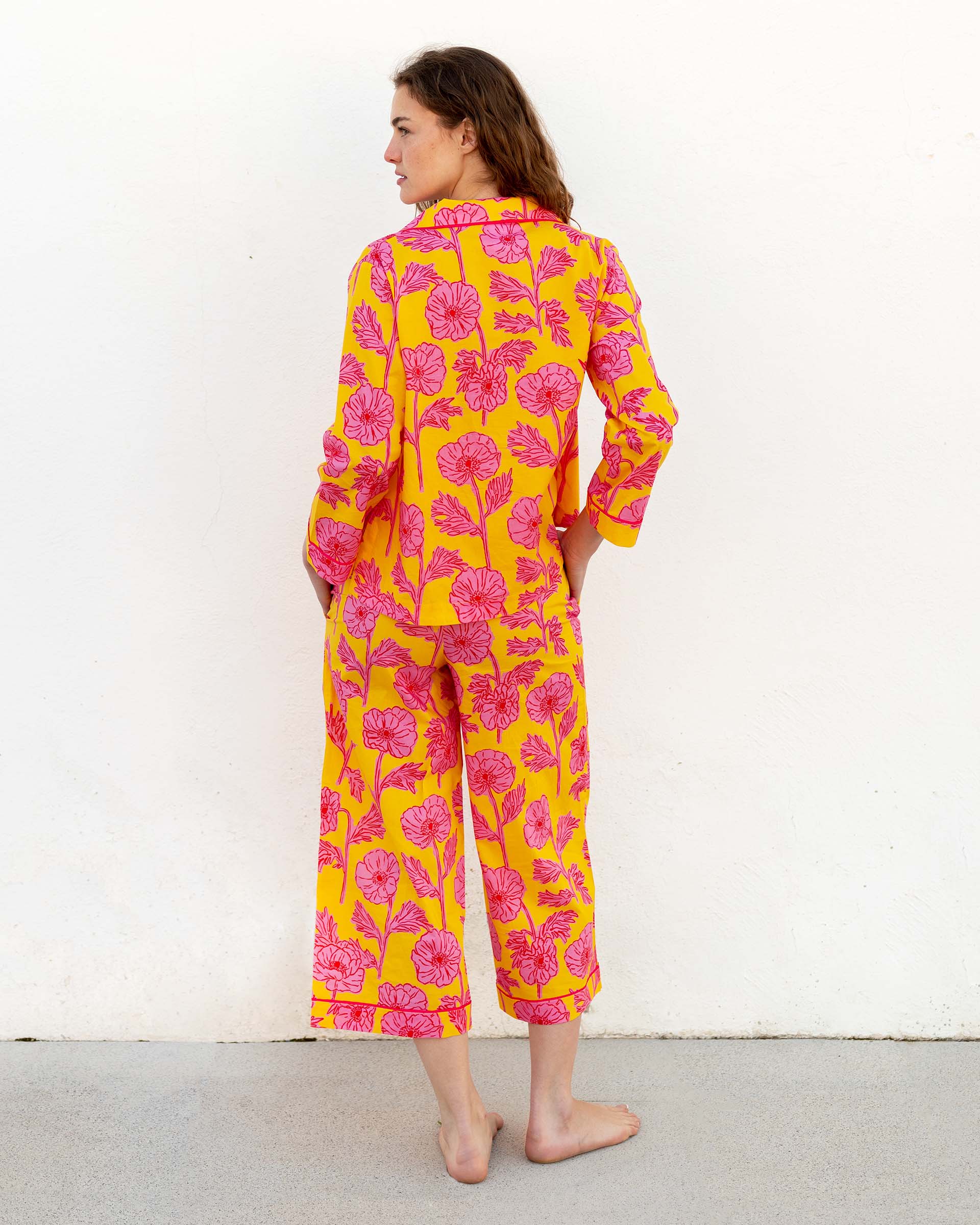 female wearing matching pajama set with pink poppy flower print backwards in front of white wall