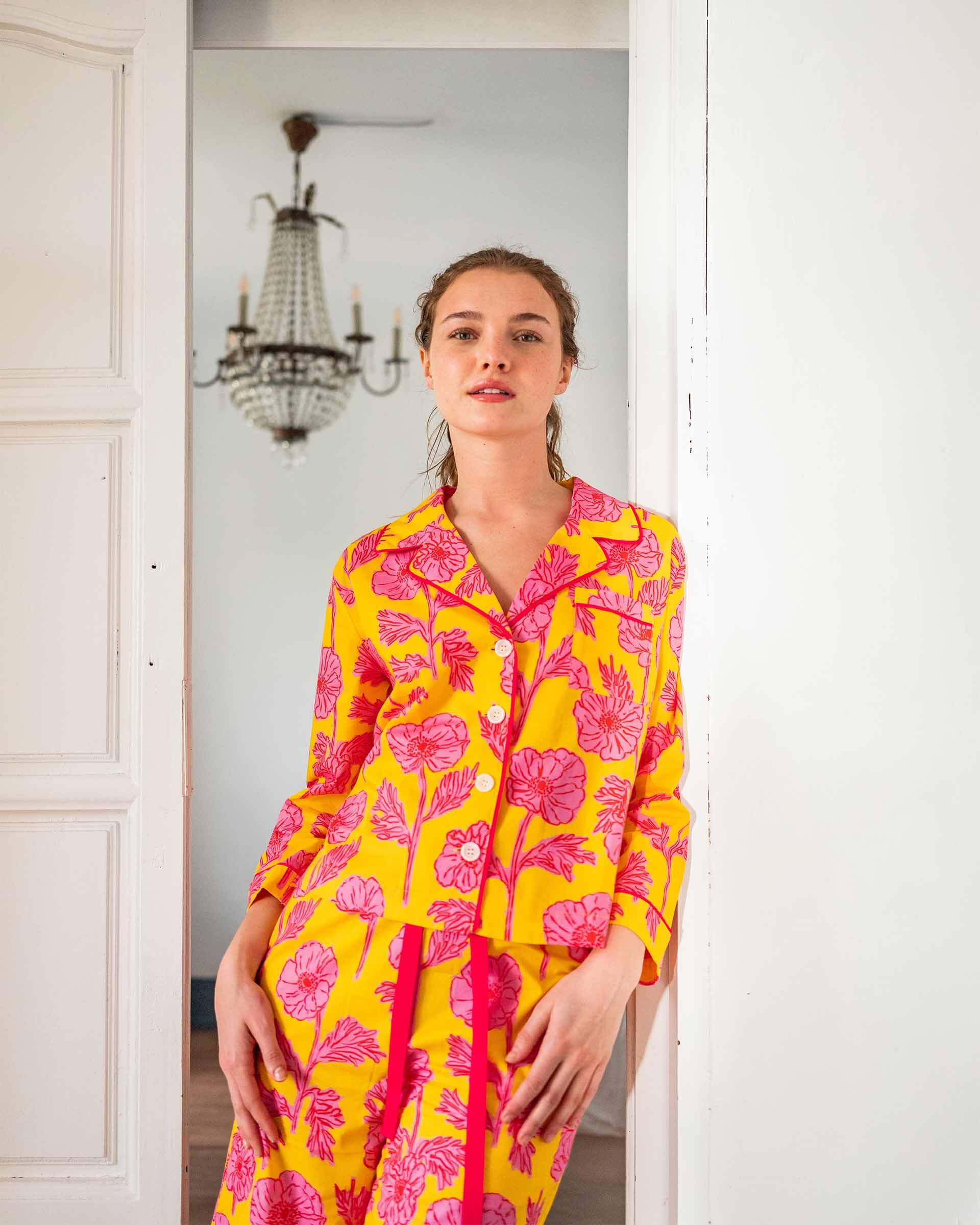 female wearing matching pajama set with pink poppy flower print leaning on a door frame