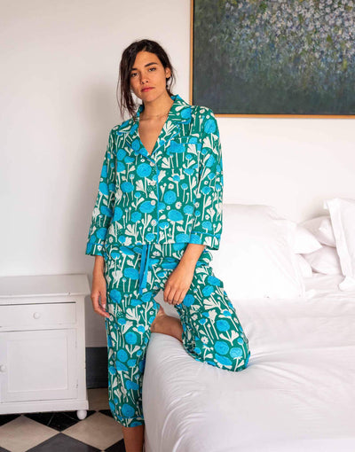 female wearing matching pajama set with ranunculus blue flower print kneeling on a bed 