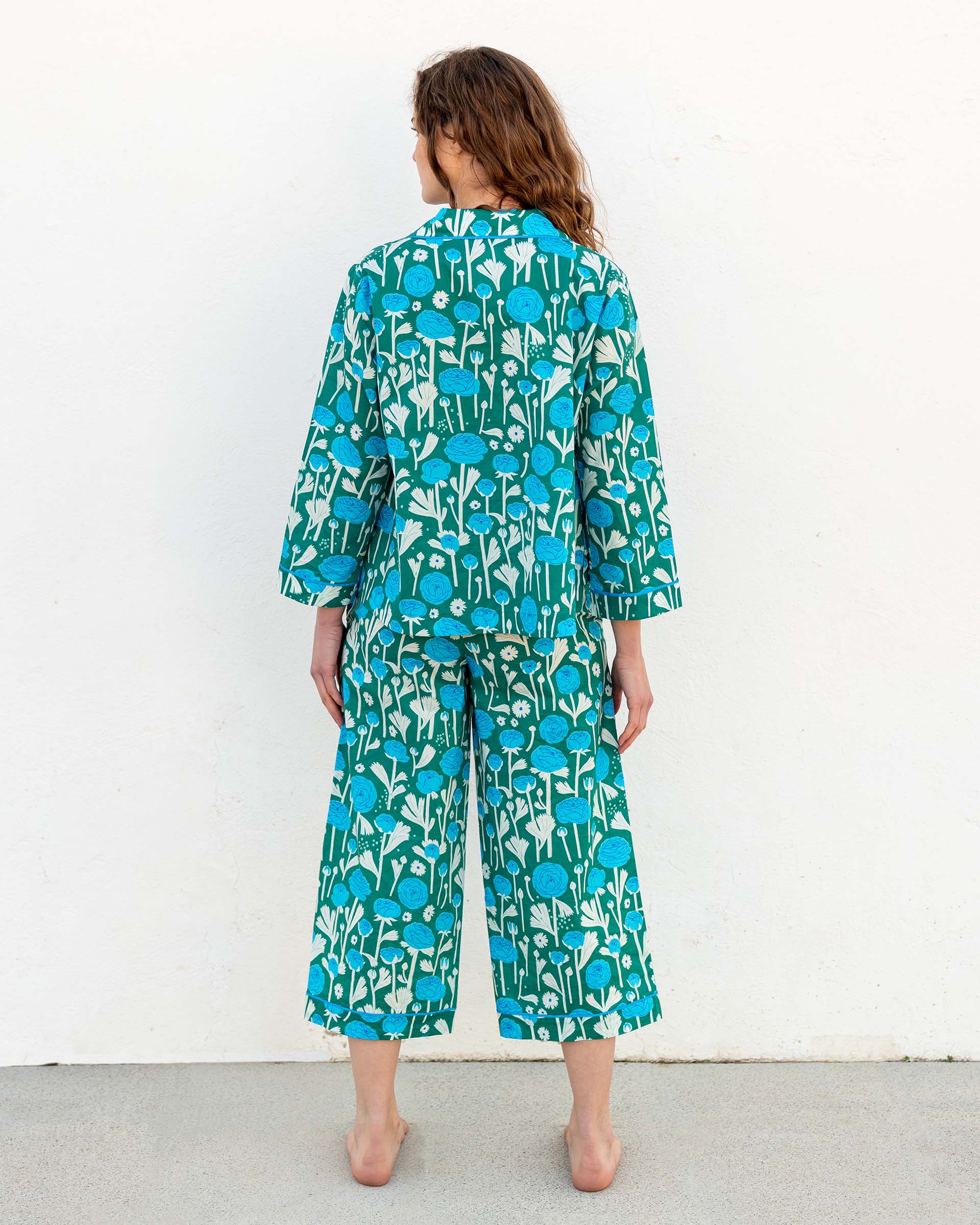female wearing matching pajama set with ranunculus blue flower print backwards on white wall