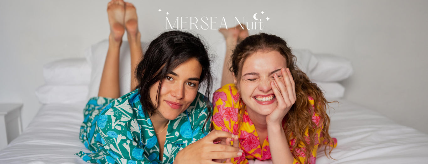 two females wearing matching floral pajama set laying down on a white bed 
