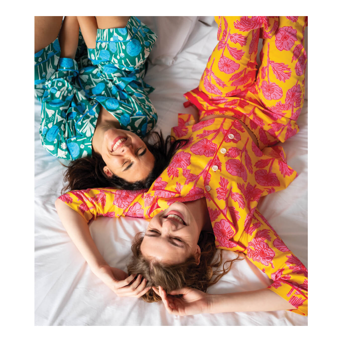 two females wearing matching floral print pajamas laying down on a bed laughing
