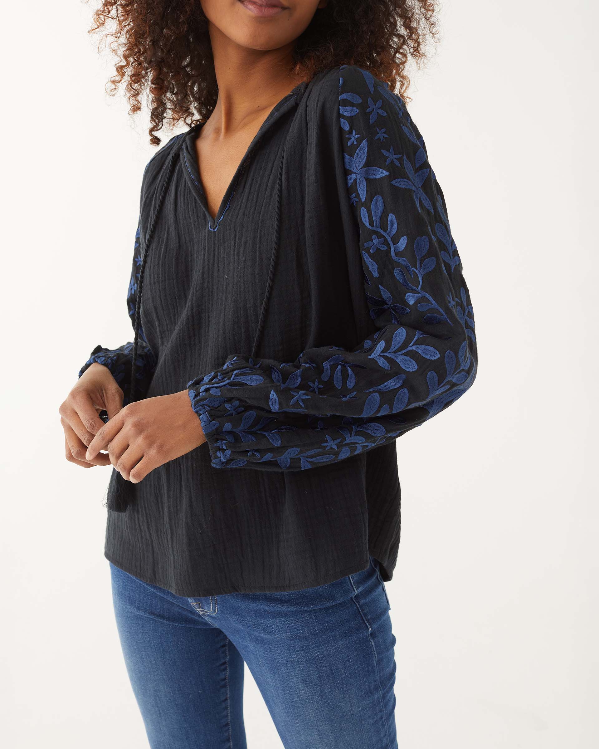 closeup of woman showcasing Mersea black v-neckline palermo blouse with embroidered sleeves and tassel ties