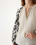 closeup of woman showcasing Mersea cream v-neckline palermo blouse with embroidered sleeves and tassel ties